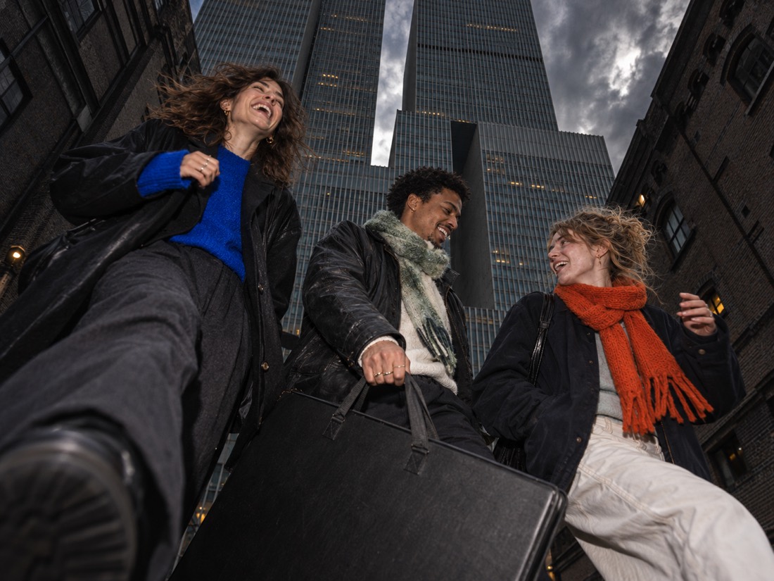 Three people walking and laughing in the street, one carrying a large portfolio case