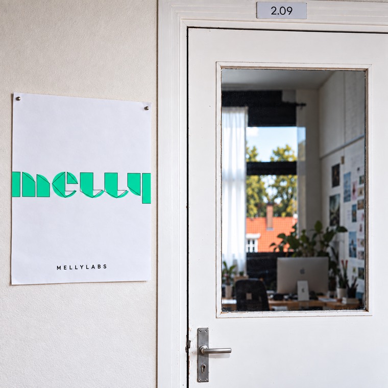 The studio door at 2.09, with the Melly Labs poster beside it and the studio visible through the glass